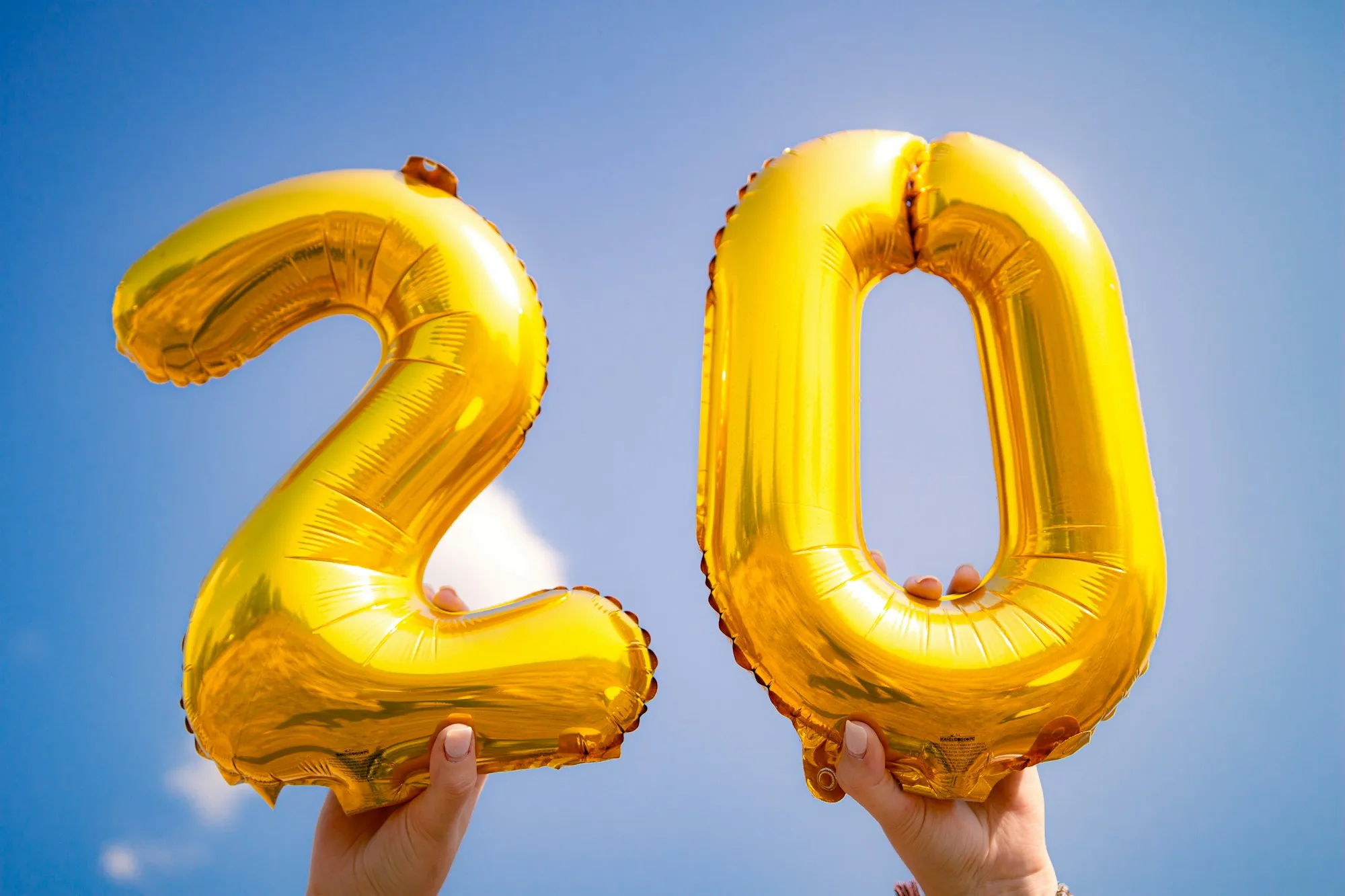 Giant gold number 2 and 0 foil balloons against a blue sky