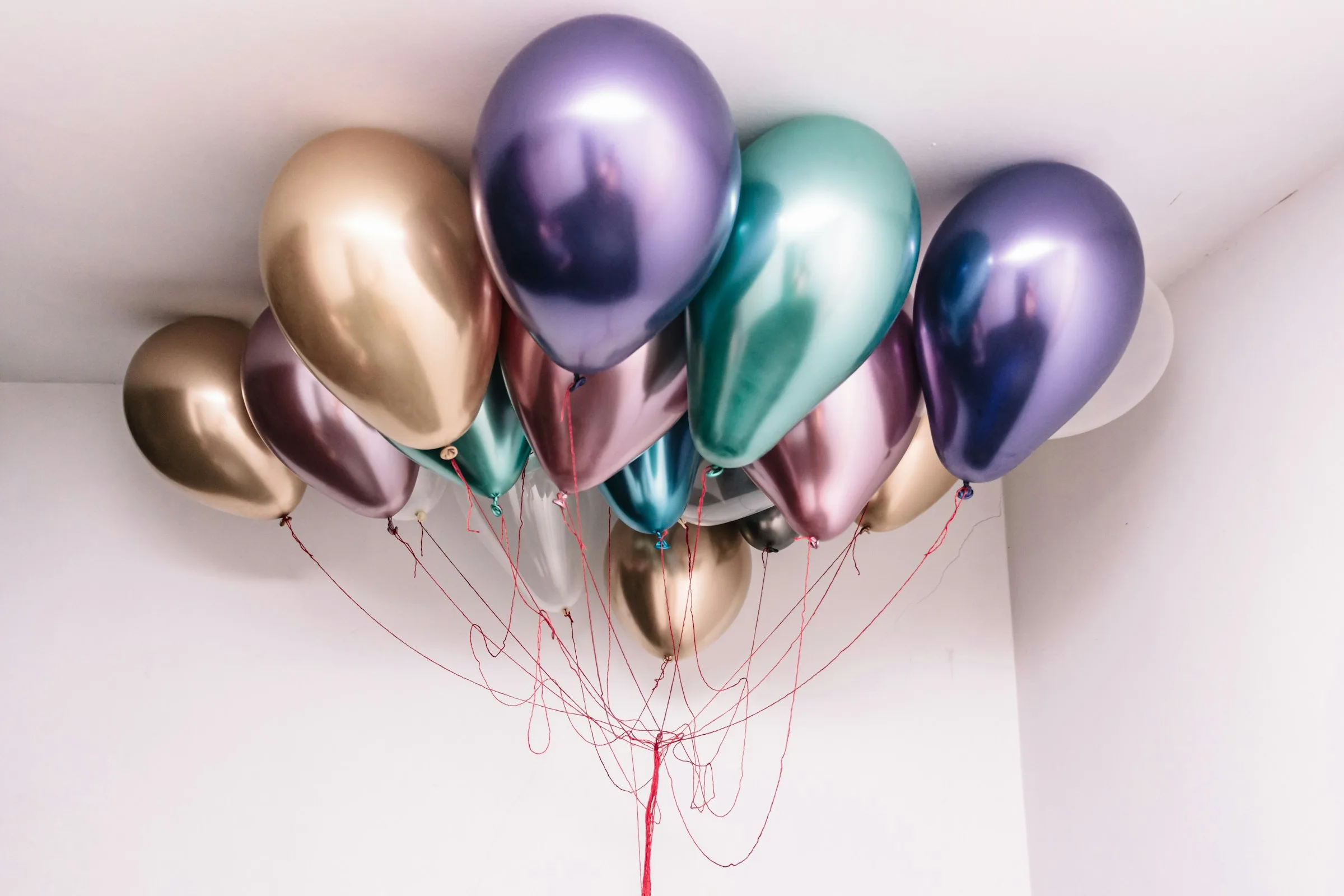 Chrome gold, purple and teal balloons floating against a white ceiling