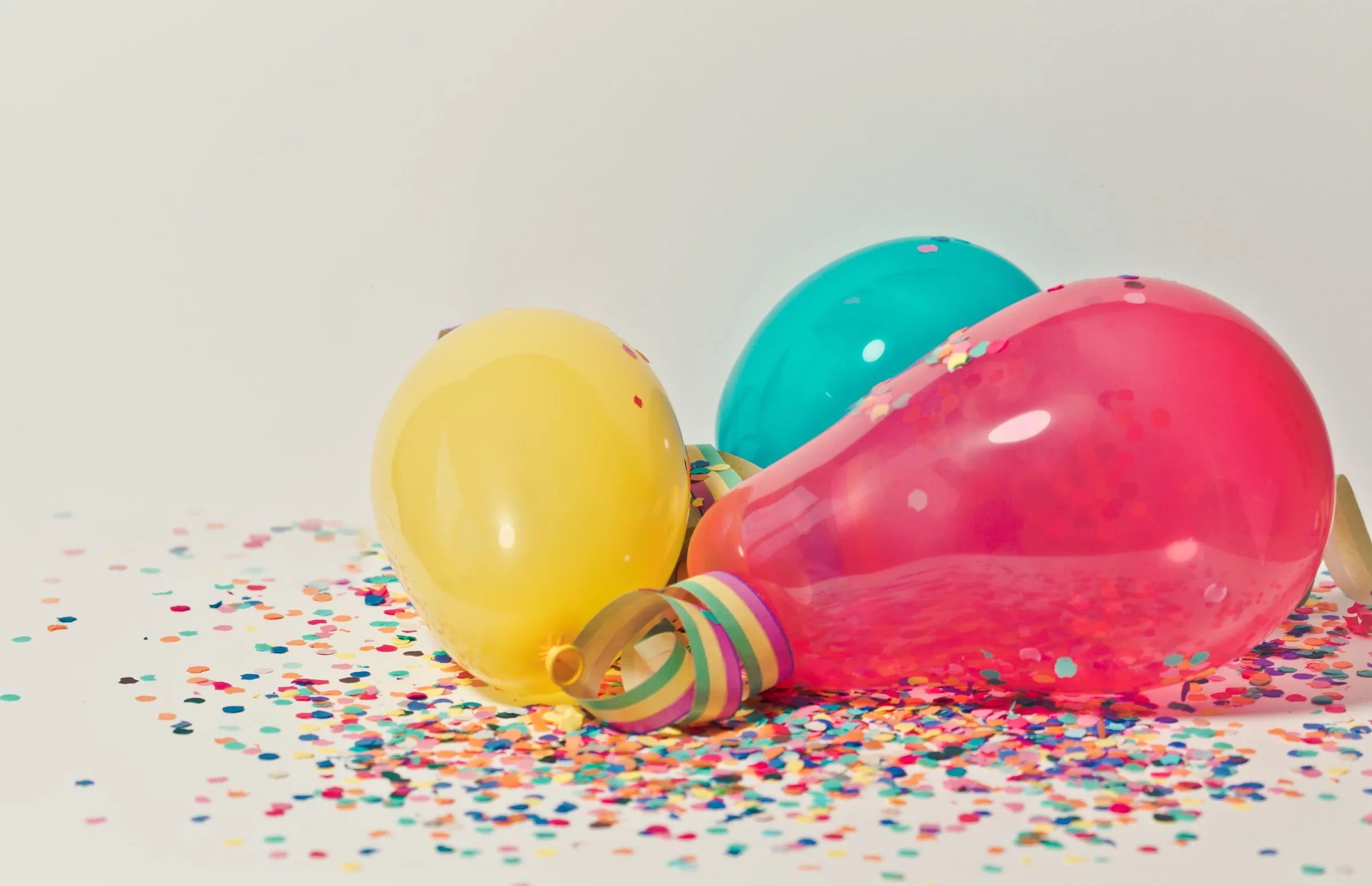 Yellow, teal and pink balloons with a curled streamer and scattered confetti