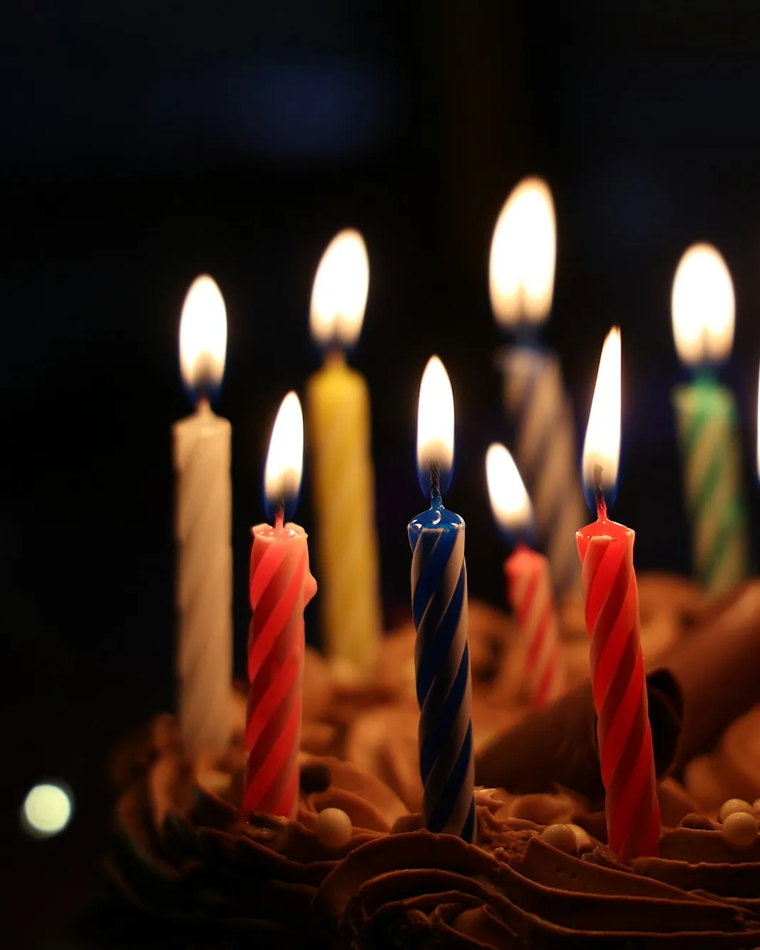 Lit birthday candles on a chocolate cake against a dark background