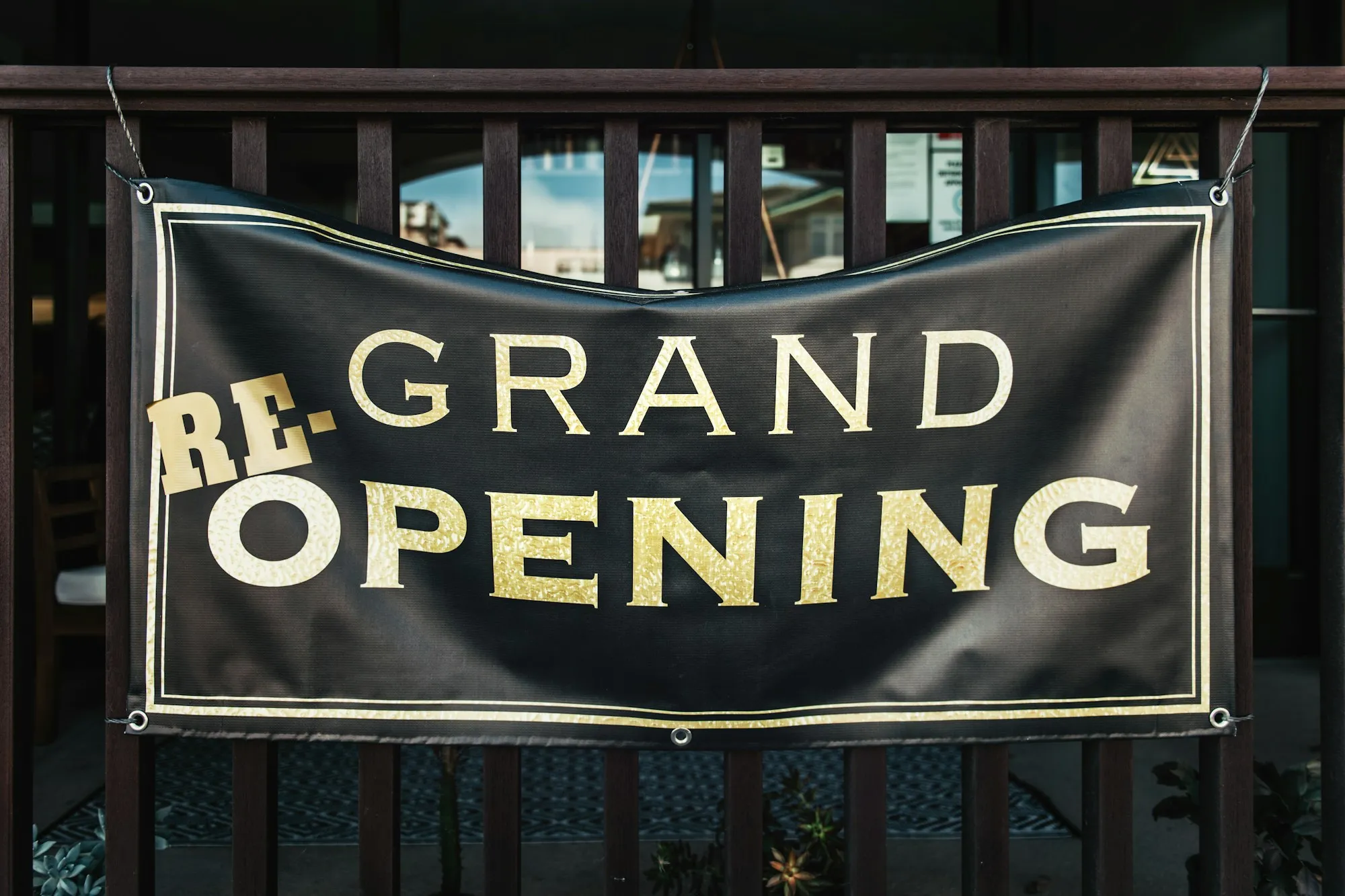 Custom vinyl banner reading Re-Grand Opening hanging on a railing