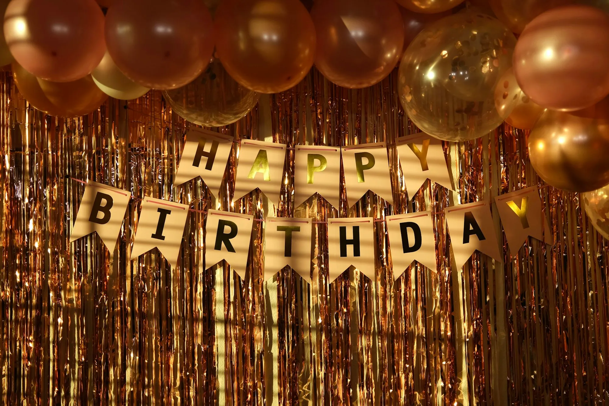 Happy Birthday pennant banner over a gold fringe curtain with balloons