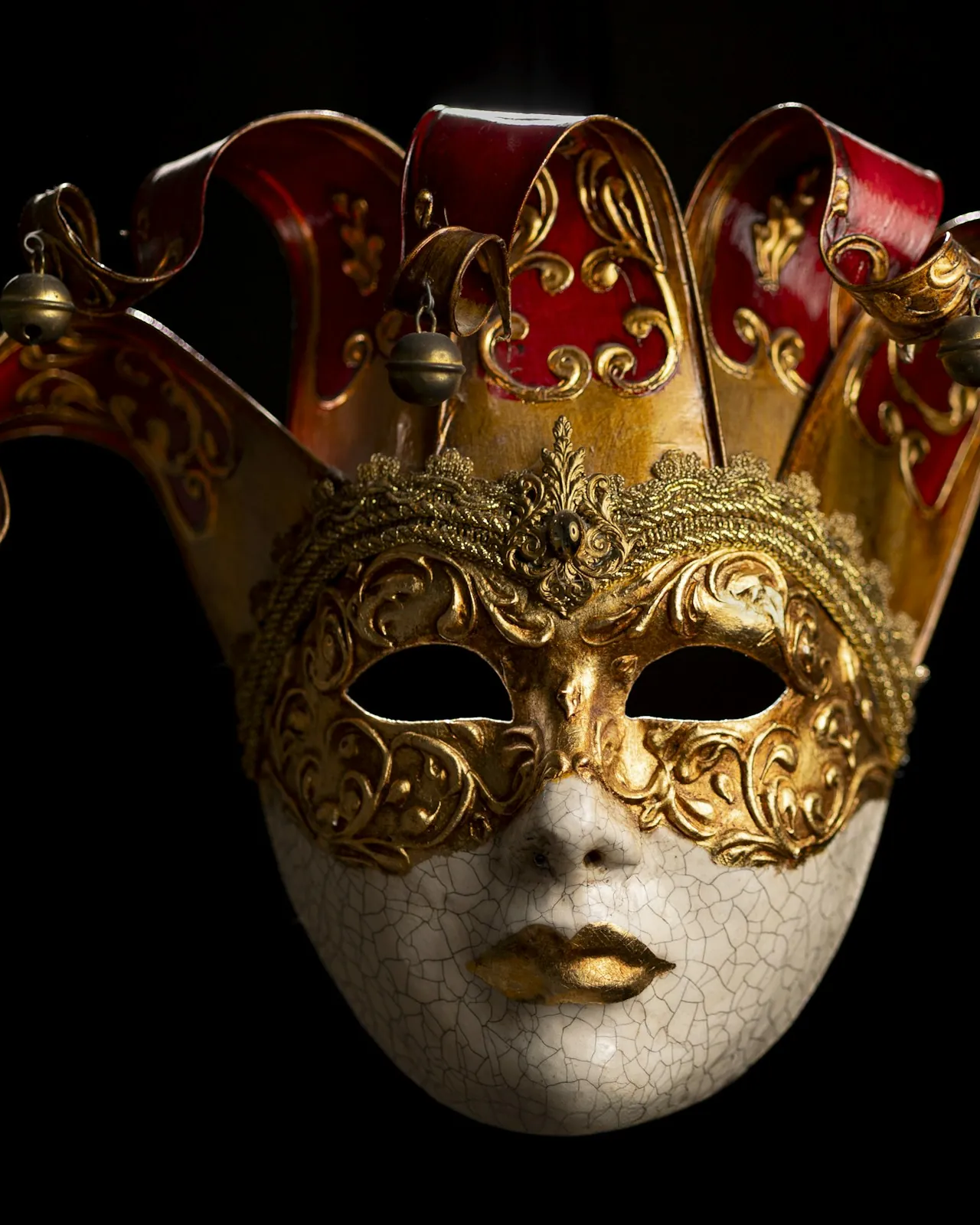 Ornate gold and red jester masquerade mask on a black background